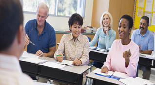 Five older adults seated at desks on which notebooks and pens sit.